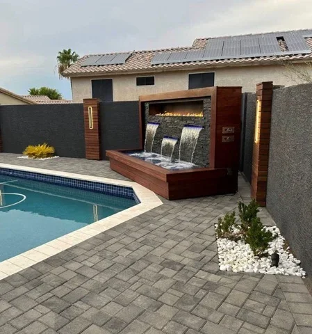 Pool patio with gray pavers, water wall feature, black metal fence, and modern hardscape design