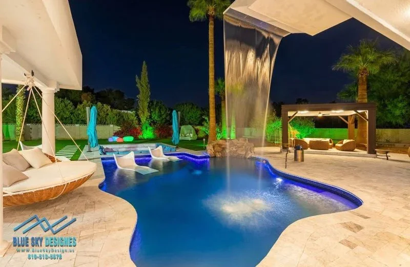 Illuminated freeform pool with travertine deck, LED lighting, pergolas, and lounge areas at night